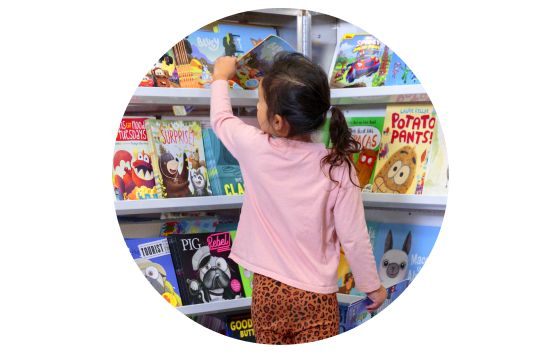 A younger students stands in front of a stocked Book Fairs book case reaching for a book