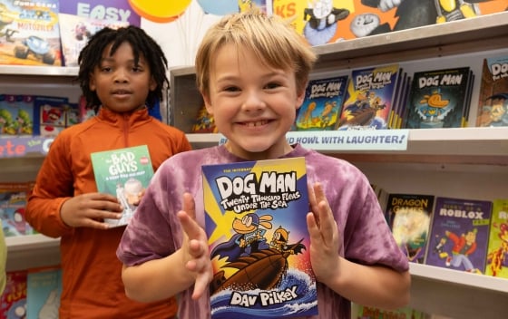 Two children showcase their books in front of Book Fair cases