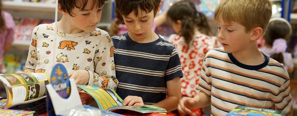 Students reading books at a Book Fair and book cases filled with vibrant titles are visible in the background