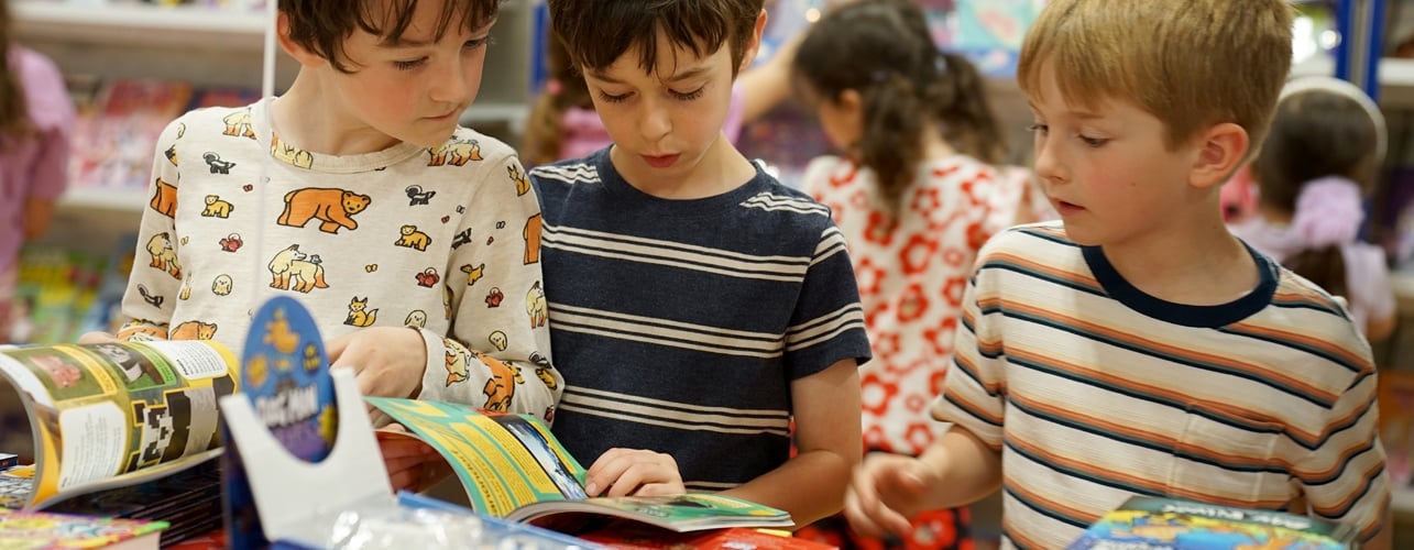 Students reading books at a Book Fair and book cases filled with vibrant titles are visible in the background