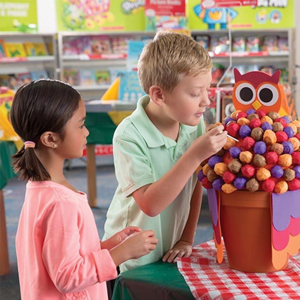 Two children pull lollipops from an owl themed basket near their Book Fair checkout